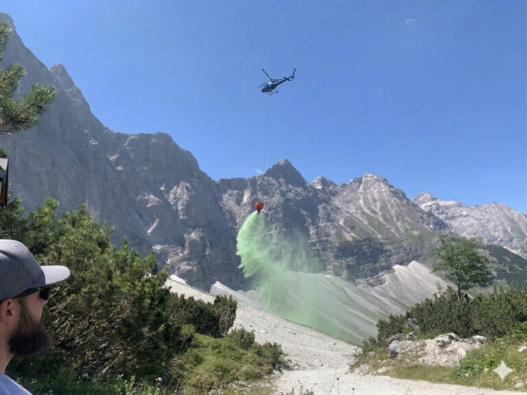 Helicopter releasing hydroseeding slurry over an alpine scree slope
