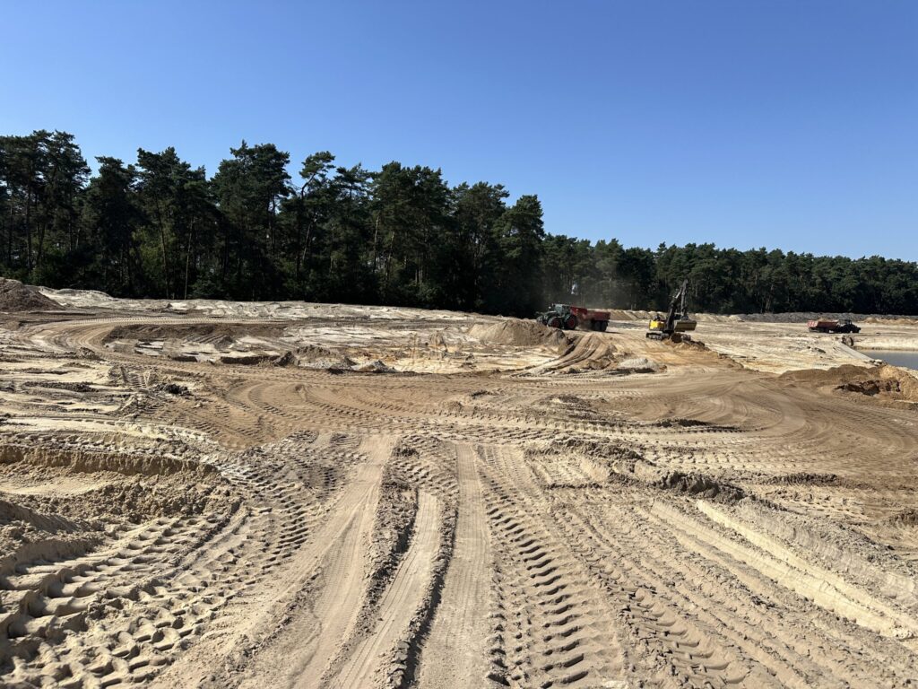 Excavator and haul trucks working in a sand quarry with heavy dust generation