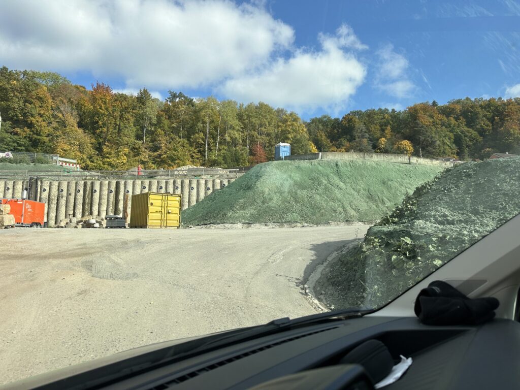 Spoil mounds sealed with green erosion control mulch beside a bored pile wall