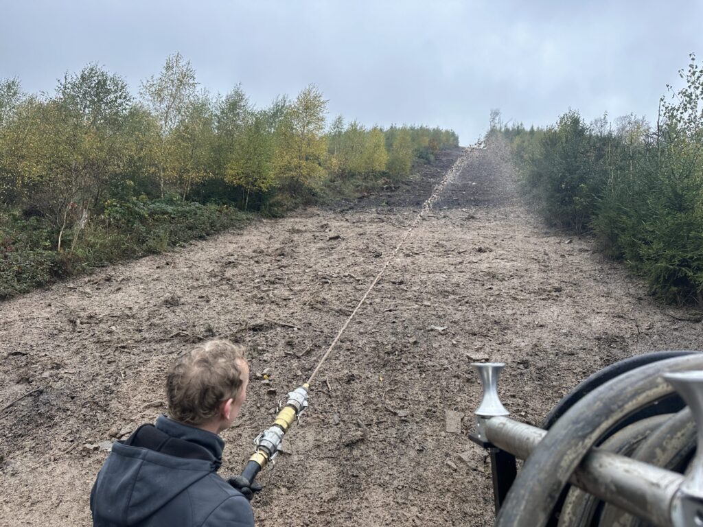 Operator spraying erosion control mulch up a bare sandy slope