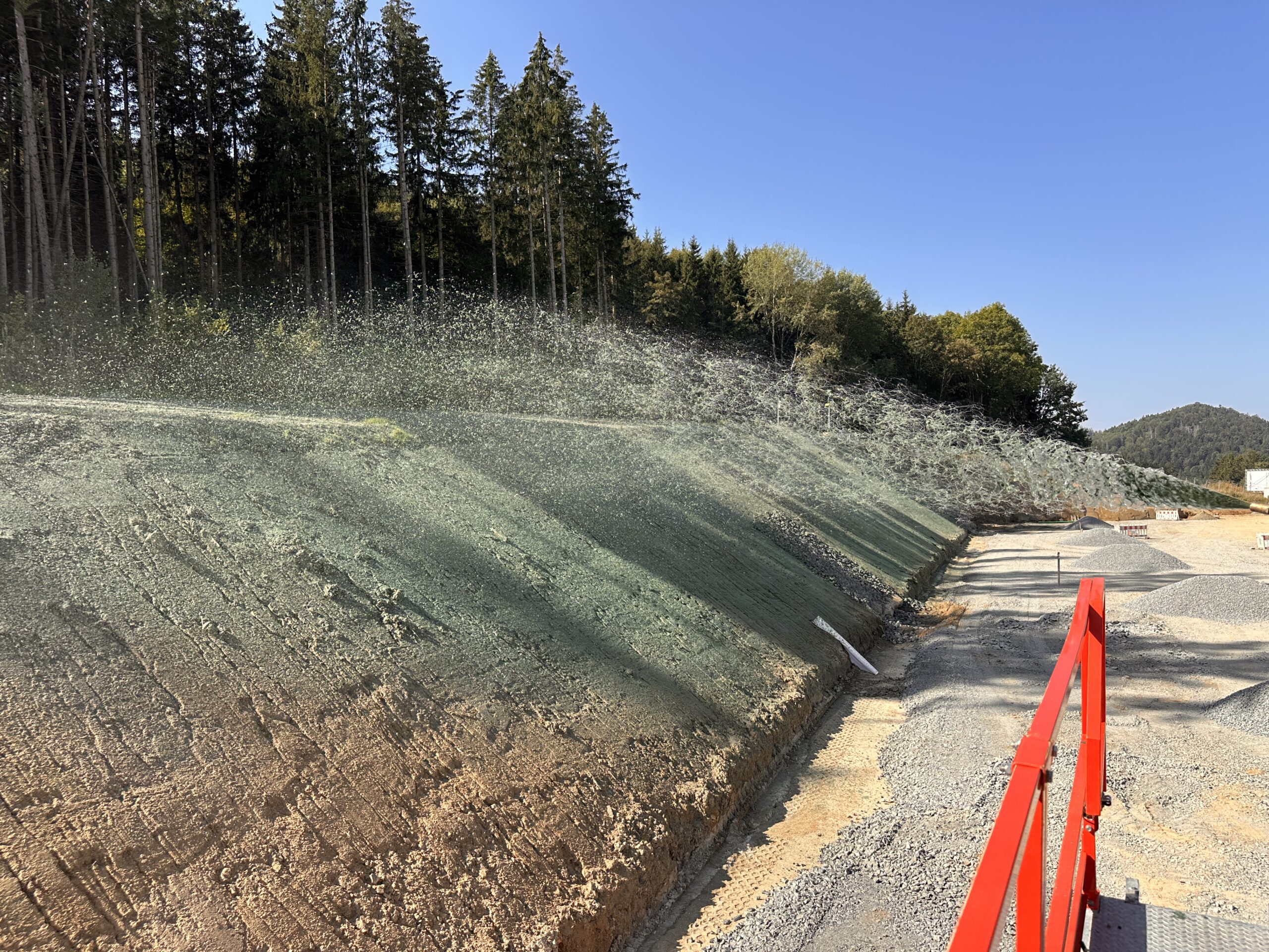 Hydroseeding slurry sprayed onto a cut slope beside a road construction site