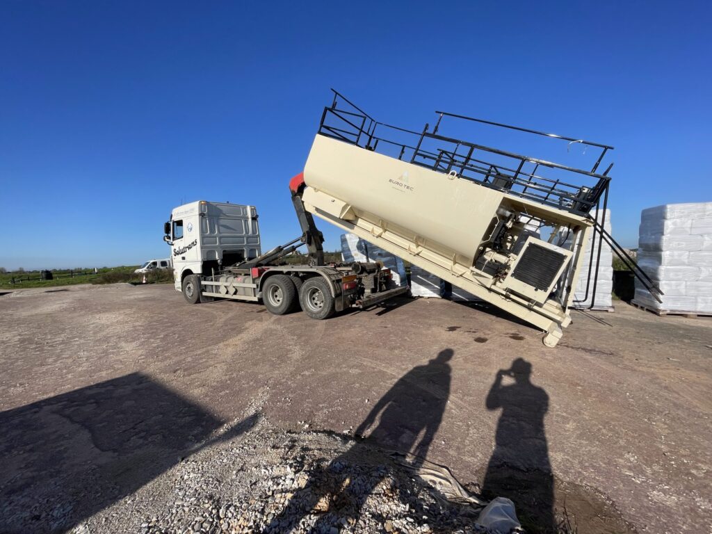 Hook-lift truck tipping a bulk silo container of hydroseeding material on site