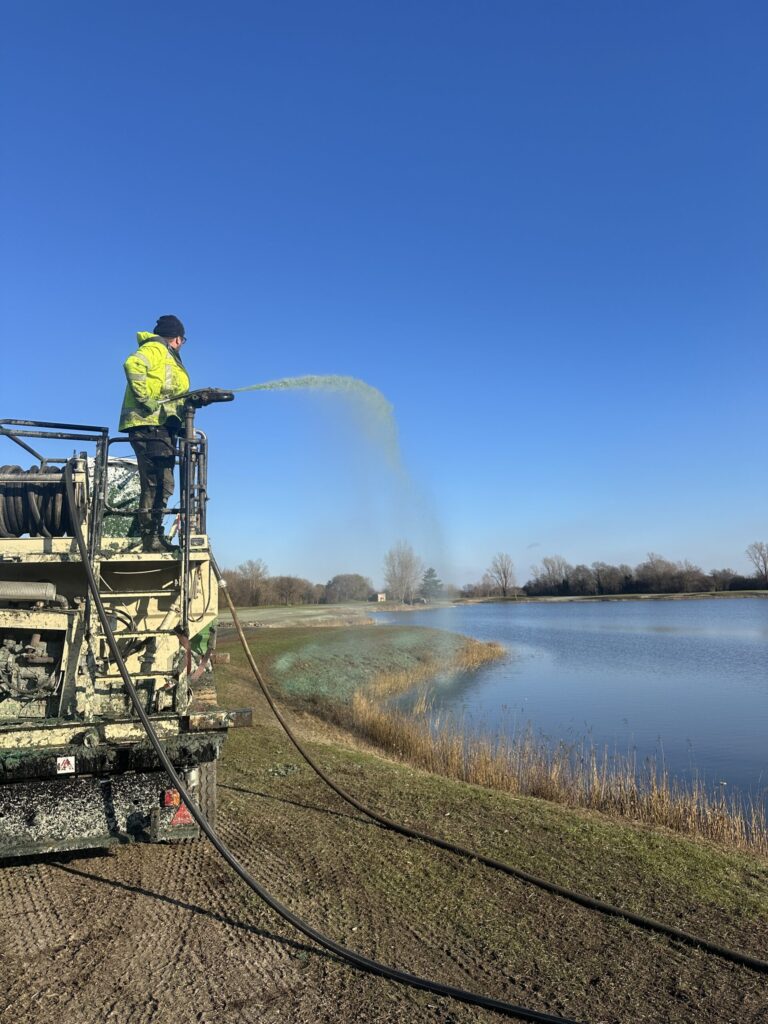 Operator spraying hydroseeding slurry onto a lakeside bank from a truck-mounted hydroseeder