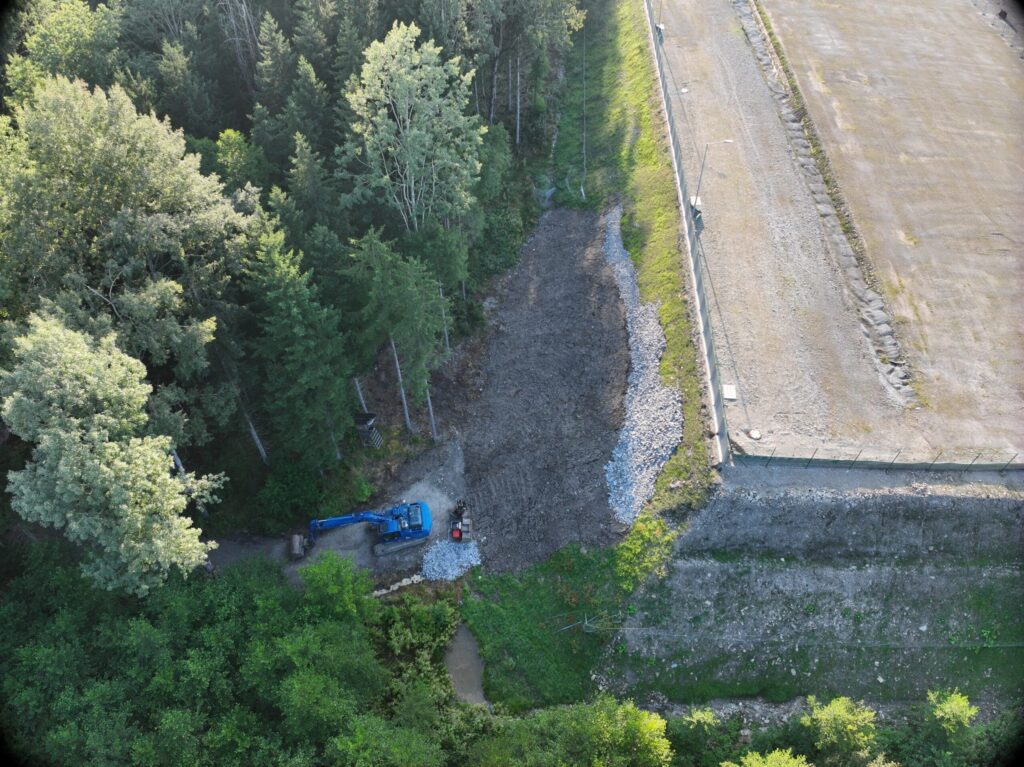 Aerial view of a landfill embankment with drainage channel and excavator