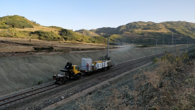 Rail-mounted spraying unit revegetating an embankment along a railway line